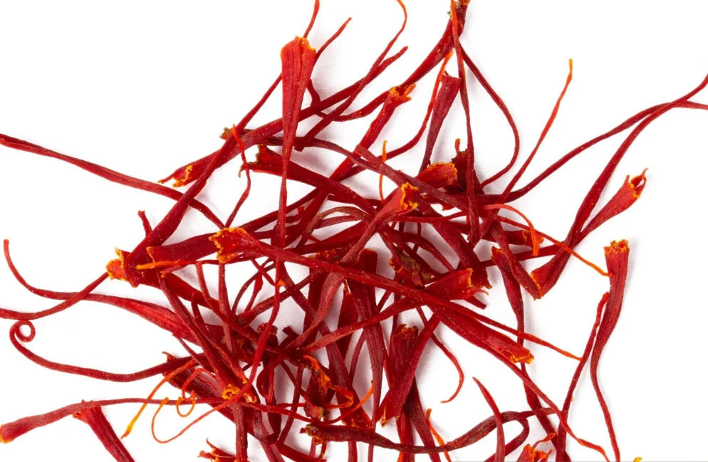 Une vue de dessus montrant un amas de stigmates de safran séchés d'un rouge profond et éclatant sur un fond blanc pur. Les filaments sont longs, fins et légèrement évasés à une extrémité, illustrant la qualité de cette épice précieuse.