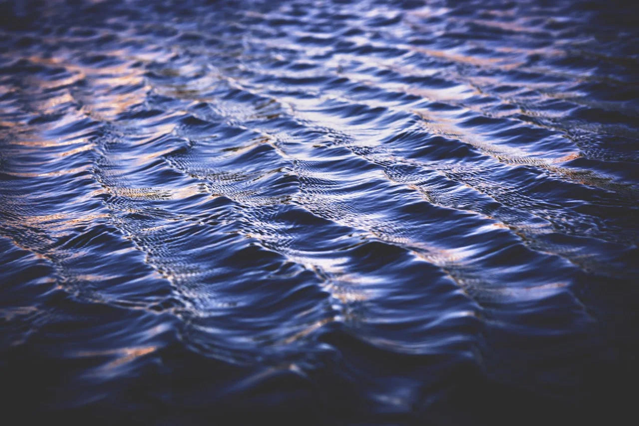Photographie en gros plan d'une eau calme et onduleuse, avec des vagues bleues profondes, évoquant la pureté et la tranquillité. Idéale pour illustrer l'origine naturelle ou la relaxation.